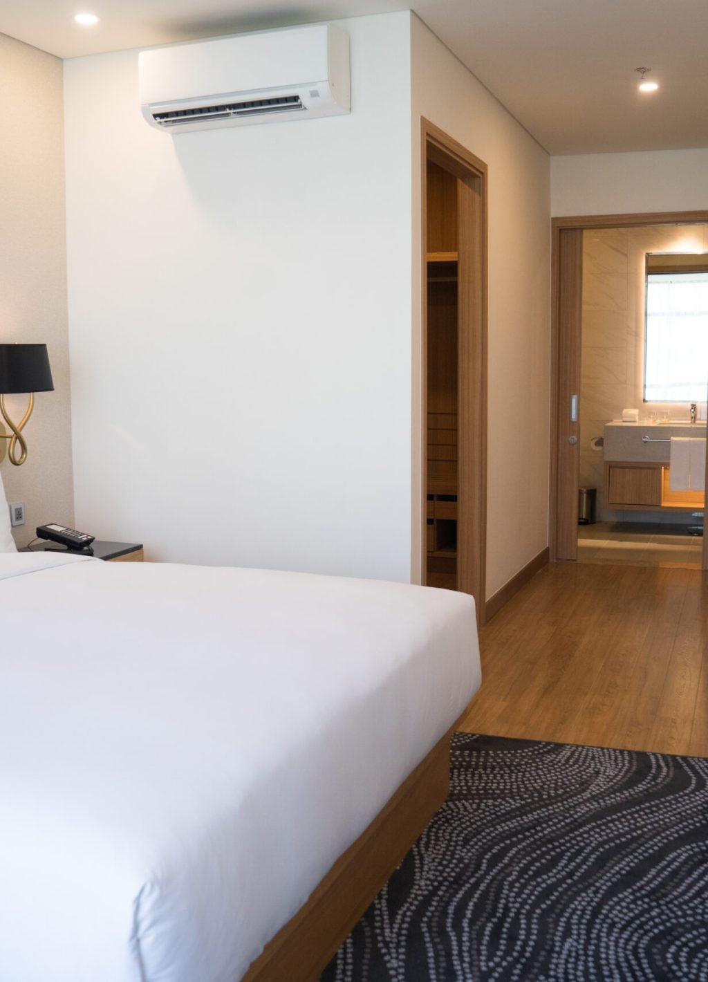 Small hotel room interior with double bed and bathroom. Double bed with white sheets complemented with wall lamp, TV and air conditioner. Hotel room concept